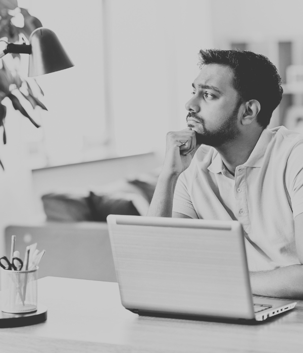 Indian man thinking, working on laptop in home office